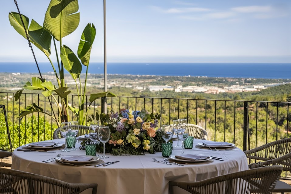 Mesa de banquete decorada con flores en la terraza de Masia Solior con vistas panorámicas al mar Mediterráneo y la costa de Barcelona.