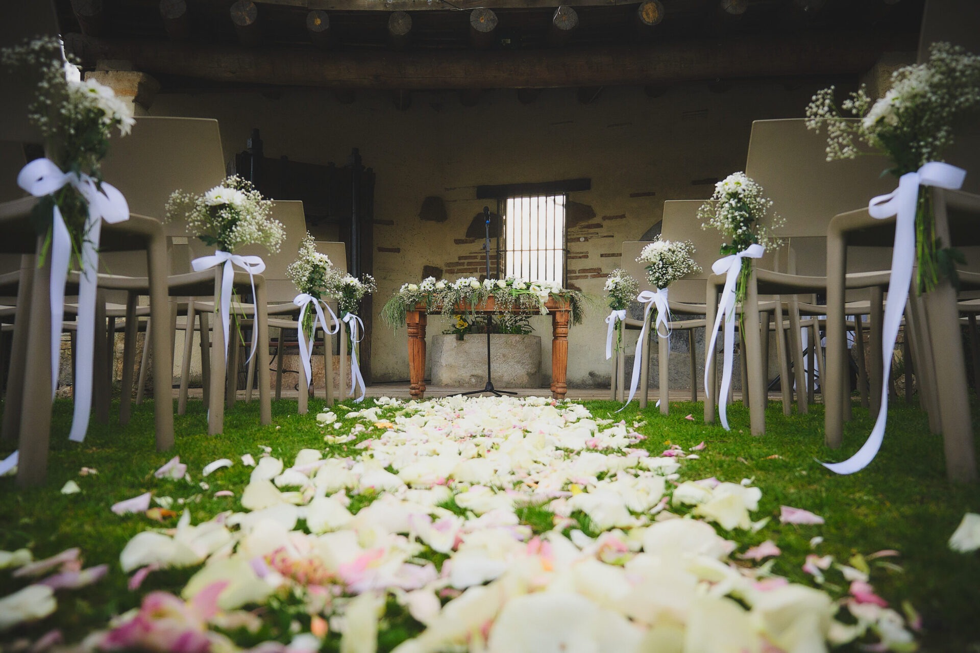 Montaje de ceremonia civil al aire libre en masía para bodas en Barcelona, con pasillo de pétalos blancos y sillas decoradas con flores.